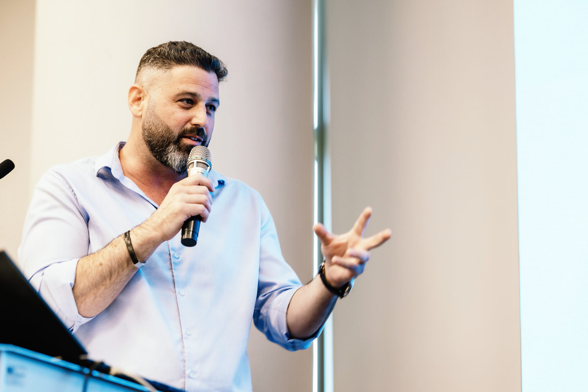 Liron Kaplan speaking into a handheld microphone while presenting to a sales team